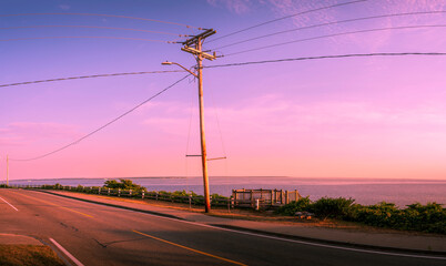 Seascape with tilted electric pole and cables on the side of the paved road on tropical backgrounds