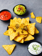 Nachos chips in bowl with sauces, dip variety. Grey stone background. Close up.