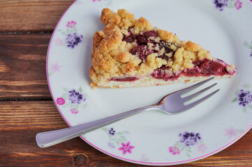 cherry crumble cake on a plate with a fork on wooden background