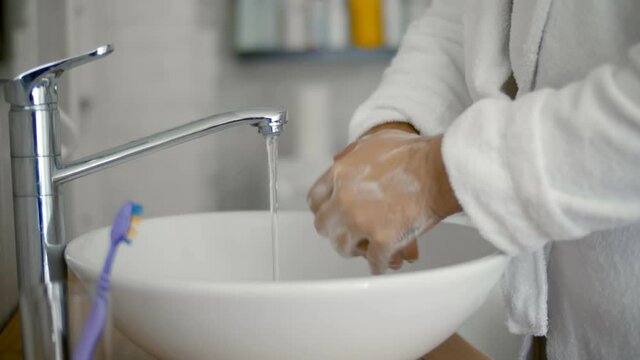 Close up of man washing hands with soap and hot water at home bathroom sink