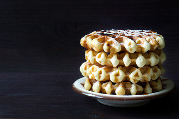 Stack of waffles covered with sugar powder on dark wooden background