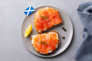 Sandwich, toast with smoked salmon and cream cheese on white plate, with Scottish flag. Grey background. Top view.