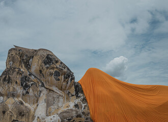Gran escultura de piedra de buda reclinado con túnica de color naranja y cielo con nubes