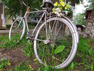 Fototapeta na wymiar An old metal grey bicycle with a bouquet of yellow flowers by a tree
