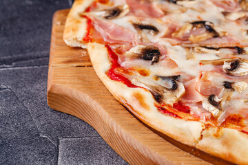 Pizza with ham and mushrooms on wooden board on dark background. Close-up