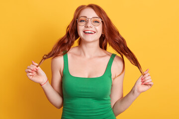 Portraits of charming red-haired girl posing with wonderful mood and lovely smile, touching her...