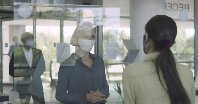 Business people arriving in corporate office lobby wearing protective face mask, receptionist giving them directions