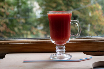 There is red tomato juice in a glass on the windowsill.