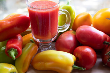 There is tomato juice in a glass. Ripe tomatoes and peppers lie nearby.