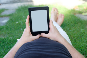 Bare foot man in grass reading e-book on digital device close up