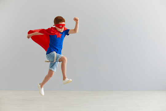 Little boy in a superhero costume jumped on a gray background. Superhero child. Kids costume.