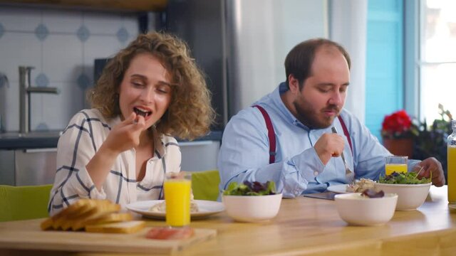 Smiling young couple having breakfast in kitchen at home