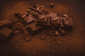 Composition of bars and pieces of different milk and dark chocolate, grated cocoa on a black background