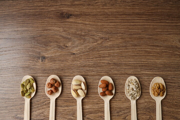 Some of the assorted nuts with pistachios, almonds, pumpkin seeds, sunflower seeds, hazelnuts in wooden spoons on a wooden background, top view. with place for text