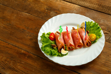 Ham rolls with cheese and garlic on a salad plate with quail eggs on a wooden table. save a place.