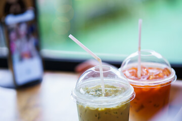 Iced green tea and iced milk tea paired together on a table by the window.