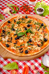 Rustic pizza with chicken meat, cheese, tomato, olive, mushrooms and tomatoes sauce, served on a wooden board for a dinner in italian restaurant background, top view. Classic Italy food. Close up