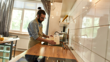 Young man, Italian cook washing chopping board in the sink in kitchen after cutting vegetables