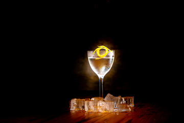 Vodka with ice and lemon in a glass on a high leg is on the bar