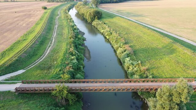 Flight above rusty road bridge above river towards small hydroelectric powerplant during summer season.