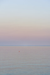 Background of a sunset by the sea with a red plastic buoy floating on the calm water in portrait format