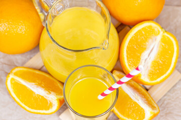 Top view of fresh orange juice in a glass with a straw and jar with fruit pieces on light wooden background.