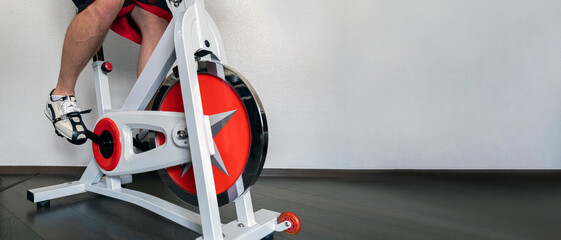 Home classes on a stationary bike. Preparing for Ironman. Men's feet spin the pedals of a home professional exercise bike. Copy space