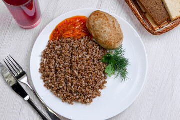 Tasty buckwheat porridge on white plate on table with meat, top view