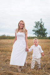 Naklejka na ściany i meble Young beautiful mother and son in white clothes posing for a photograph in a wheat field