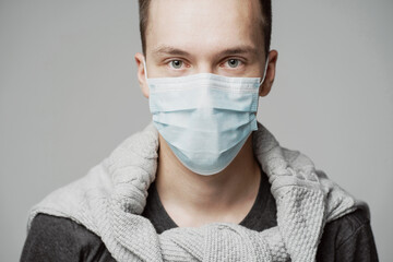 thoughtful man of Caucasian appearance, looks into each other's eyes. portrait of a young man in a blue mask that protects against the covid-19 pandemic. grey background photo Studio