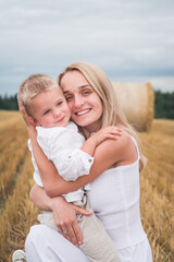 Young beautiful mother and son in white clothes posing for a photograph in a wheat field
