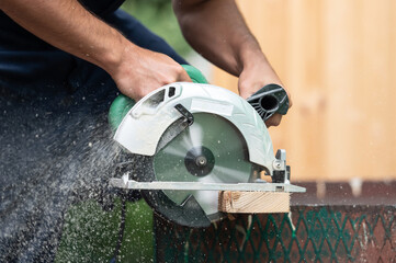 Man using circular saw to cut off wood. Diy at backyard - obrazy, fototapety, plakaty