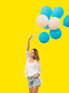 Young woman jumping with blue and white helium balloons isolated on yellow