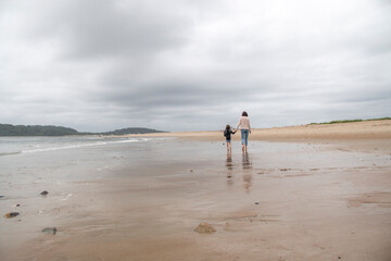 Mother and daughter walking down a sandy beach in the summer