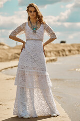 Fototapeta na wymiar A beautiful model poses on a deserted beach in a white lace dress on a Sunny day