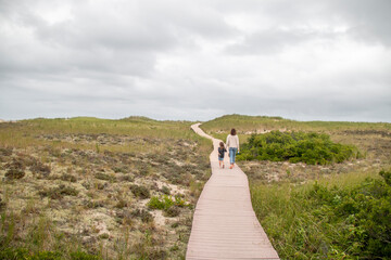 Mother and daughter walking down a wooden path to the beach