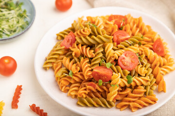 Tortiglioni semolina pasta with tomato and microgreen sprouts on a white wooden background. Side view, selective focus.