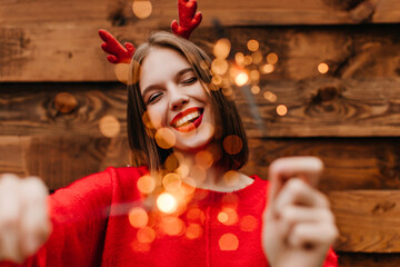 Blissful female model enjoying winter holidays. Carefree girl posing with bengal lights and laughing.