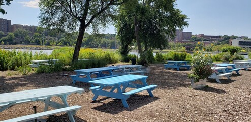 Light blue picnic tables on the shore of the Harlem River on a sunny day in Sherman Creek Park in uptown Manhttan's Inwood neighborhood. 