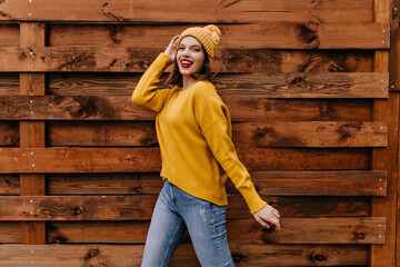 Woman in yellow sweater and jeans dancing on wooden background. Amazing girl with cheerful smile looking to camera.