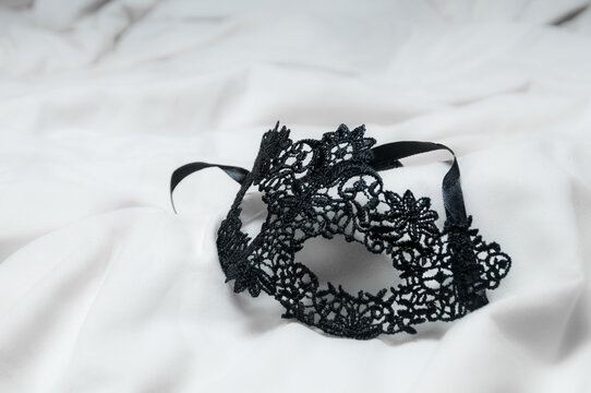 
Delicada máscara de encaje negro y seda para juegos de seducción entre las sábanas blancas de la cama de un hotel después de una fiesta secreta anónima