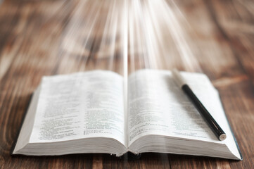 Open Bible book on a wooden table. Light over the book.