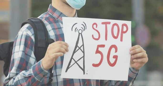 Unrecognizable man in face mask holding Stop 5G banner outdoors. Male Caucasian demonstrator protesting against harmful radioactive pollution causing Covid-19 disease. Cinema 4k ProRes HQ.