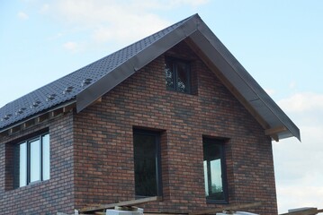 attic of an unfinished brown brick house with an empty windows under a tiled roof of blue sky