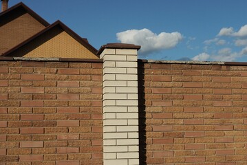 part of a wall of a fence made of white and brown bricks on the street against a blue sky