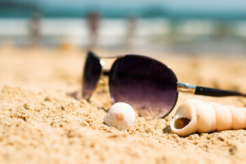 Sunglasses lying on a tropical sandy beach with seashells and stones. Sunglasses on the beach. Nice sea view. Vacation, travel concept