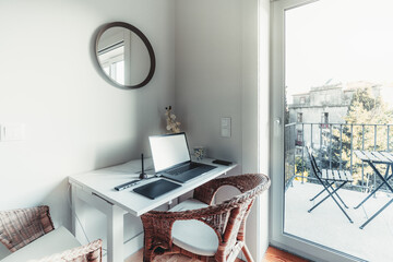 Wide-angle view of a bright room next to the balcony door, in a residential apartment with a work-table; on the table there are: opened laptop with a blank screen, multimedia adaptor, graphic tablet