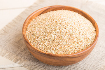 Wooden bowl with raw white quinoa seeds on a white wooden background. Side view, selective focus.