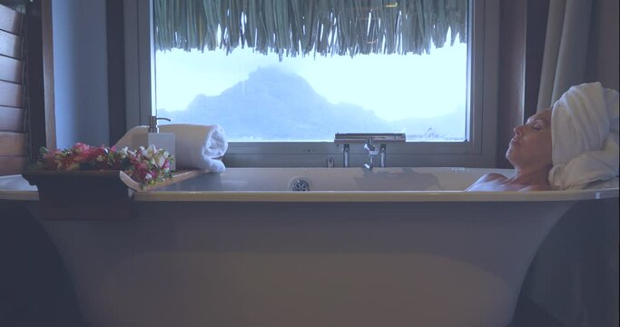 Pretty woman relaxes in a hot batch tub near a steam covered window with a mountain view. Self care spa treatment. 