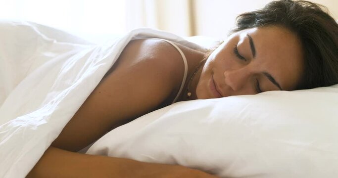 Authentic close up shot of an young brunette woman is sleeping peacefully wrapped in warm duvet blanket in a cosy bed in a bedroom. Concept of comfort, relax,sleeping,health, bedding, softness, dreams